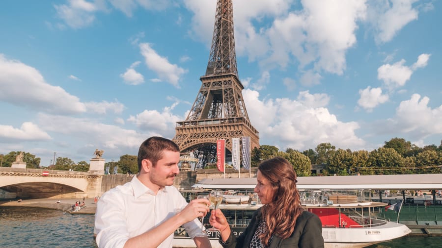 un couple sur un bateau trainquant avec un verre de champagne à la main, avec la tour eiffel derrière