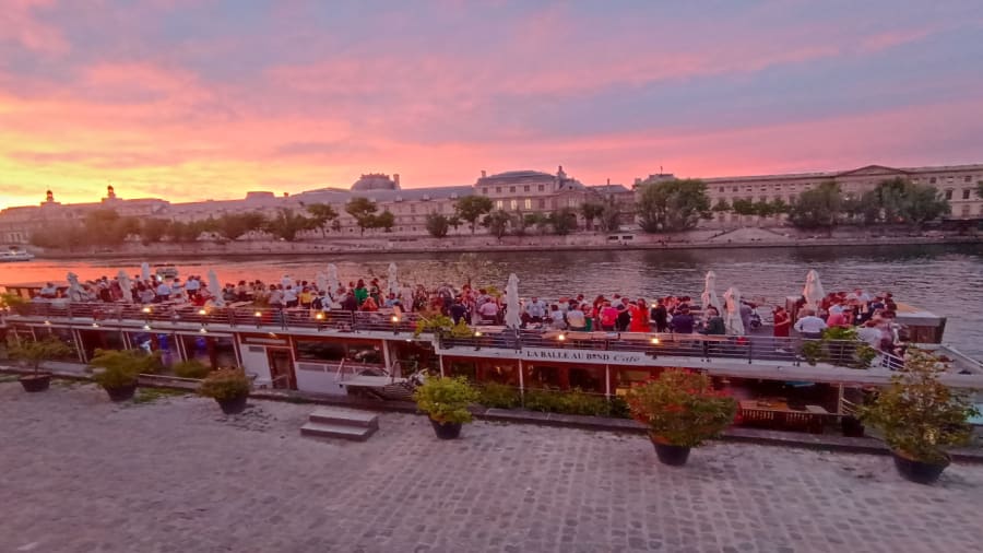 une péniche à quai avec des personnes qui célèbrent au coucher de soleil à paris