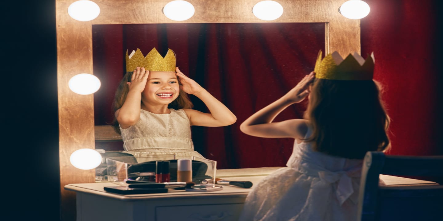 Petite fille avec une couronne se regardant dans le miroir d'une loge