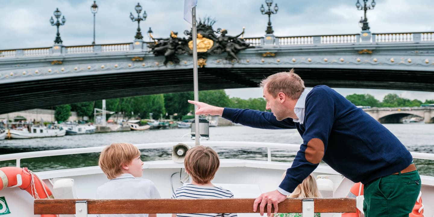 homme pointant du doigt quelque chose pour le montrer à des enfants assis sur le toit d'une péniche