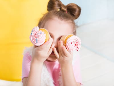 petite fille qui cache ses yeux avec deux cupcakes