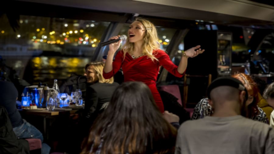 photo d'une chanteuse avec un micro entrain de chanter au milieu des tables, dans une péniche navigant sur la seine à Paris la nuit