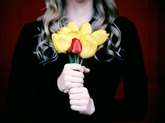 Woman holding a bouquet of yellow flowers and one red flower