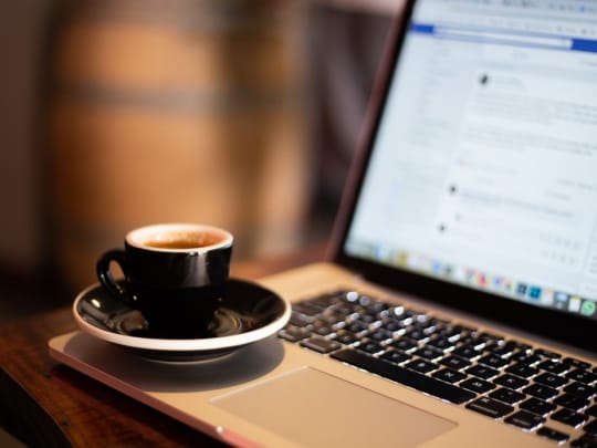 A small cup of coffee sitting on the edge of laptop