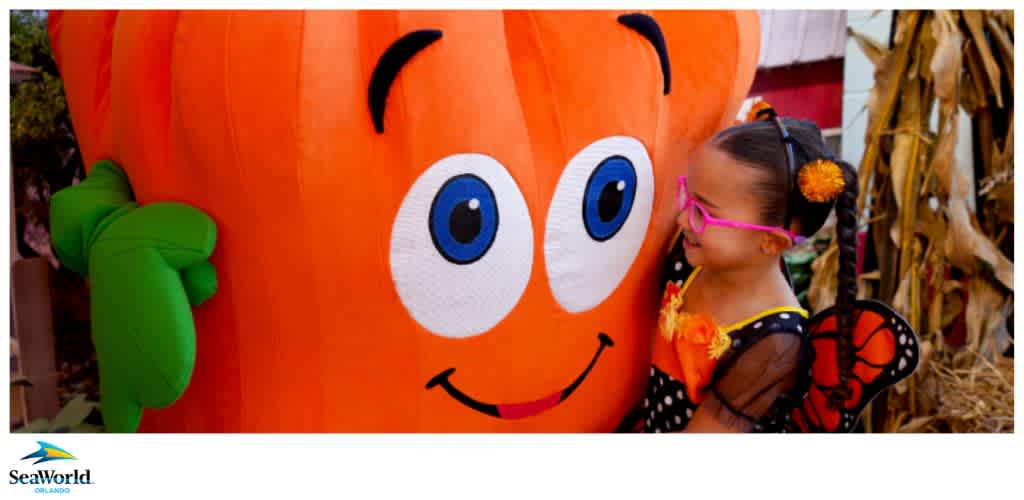 A young girl in a butterfly costume hugs a large inflatable pumpkin at SeaWorld Orlando.