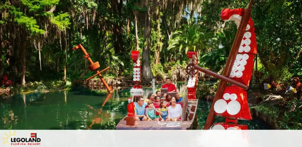 Tourists on a boat ride at LEGOLAND Florida with Lego giraffe and tree sculptures.