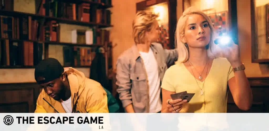 Image Description: This is a promotional image for "The Escape Game LA". It features three individuals engaged in what appears to be an escape room activity. On the left, a person wearing a black cap and a yellow jacket is leaning forward, attentively examining something out of the camera's view. In the middle background, another person is looking away from the camera, possibly focusing on clues within the room. On the right, a person with blonde hair styled in a bob is holding a flashlight in one hand and a smartphone in another, casting light onto an object to inspect it closely. The room is decorated with shelves filled with books and framed artwork, contributing to the ambiance of an enigmatic setting for the escape game.

At FunEx.com, we're committed to providing the thrill-seekers among you with unforgettable experiences at the lowest prices - don't miss out on our exclusive discounts and savings on tickets to "The Escape Game" and other exciting adventures!