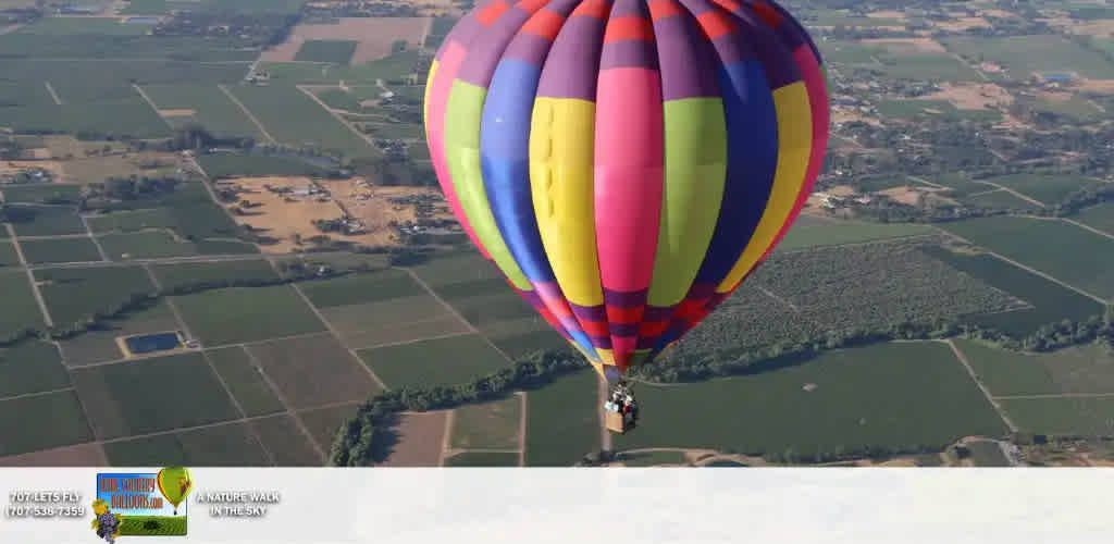 This image features a vibrant hot air balloon floating above a pastoral landscape. The balloon occupies the right side of the frame and is adorned with bold stripes of red, yellow, blue, purple, and green, creating an eye-catching contrast with the clear blue sky. Below, the balloon is a panoramic view of the countryside, with a patchwork of fields in various shades of green and brown, divided by lines that hint at roads or pathways. Several scattered buildings can be seen among the fields, indicating a rural setting. The balloon's basket is visible beneath the colorful envelope, carrying what appears to be passengers enjoying the view from high above.

At FunEx.com, we offer the thrill of adventure with the savings you desire. Discover the lowest prices on tickets for hot air balloon rides and more, ensuring your sky-high escapade is as affordable as it is unforgettable.