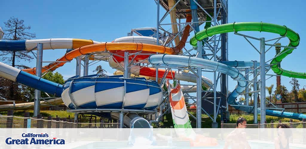 Experience the excitement at California's Great America with a snapshot of the vibrant water slides at their water park. The image captures a sunny day filled with twisting tubes in blue, orange, green, and white, creating a playful labyrinth against a clear sky. The water park's lively atmosphere invites visitors for a refreshing and joyful time.