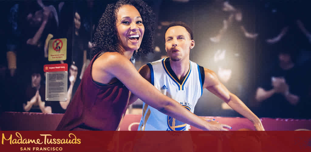 Description: The photograph captures a joyful moment at Madame Tussauds San Francisco, featuring a person posing with an incredibly lifelike wax figure of a basketball player wearing a Golden State Warriors uniform. The individual posing has a broad smile, and it appears as though they are engaged in a playful interaction with the wax statue, which is positioned as if it is dribbling a basketball. The surroundings suggest a festive atmosphere with blurred figures in the background, indicating other visitors and possibly other exhibits nearby. Ambient lighting contributes to the lively ambiance of the scene. Emblazoned at the top is the Madame Tussauds logo, confirming the setting.

FunEx.com is excited to offer special discounts on tickets to amazing attractions like Madame Tussauds, ensuring you experience the fun at the lowest prices possible.