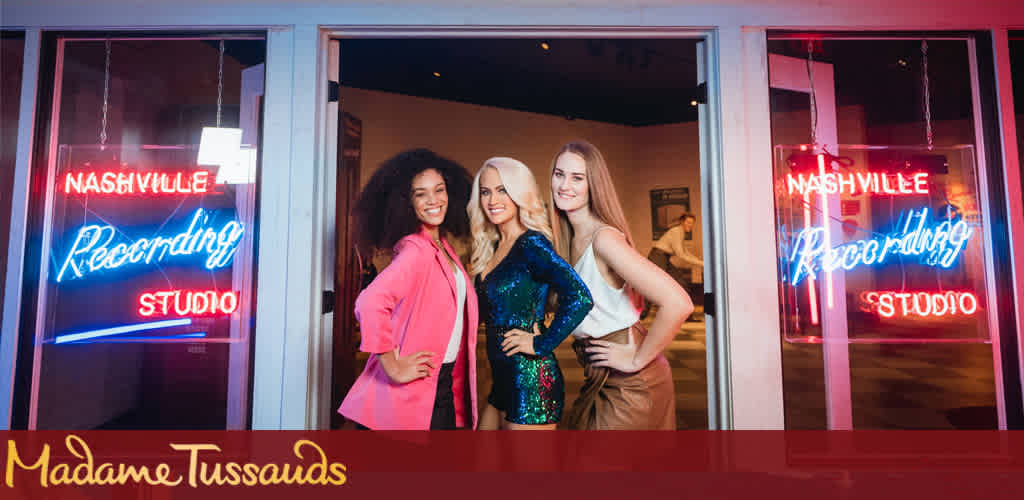 This image features three smiling individuals posing together inside Madame Tussauds, standing in front of a window. The person on the left has curly hair and is wearing a pink blazer, the middle individual has straight, blond hair and dons a sequined blue dress, while the person on the right has long, straight hair and is clad in a cream-colored sleeveless top. Bright neon signs that read "Nashville Recording Studio" flank them on both sides of the window. The Madame Tussauds logo can be seen at the bottom center of the photo.

At FunEx.com, we're excited to offer exclusive deals to make your next adventure unforgettable. Don't miss out on the savings - shop with us for the lowest prices on tickets to top attractions like Madame Tussauds!