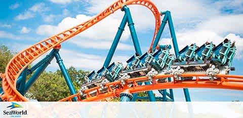 A roller coaster with orange tracks inverts riders against a clear sky.