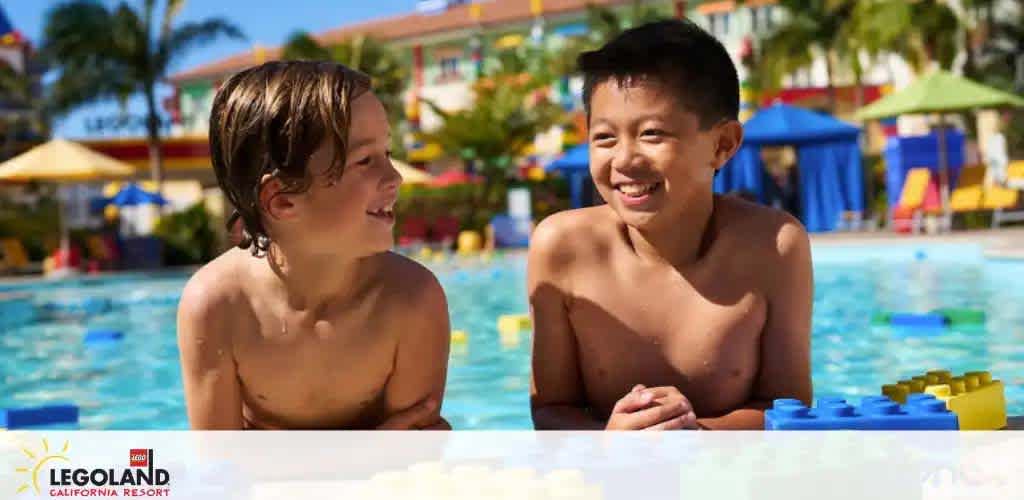 Image shows two joyful children in a pool under a sunny sky at LEGOLAND California Resort. One child is looking at the other with a smile. In the background, bright pool toys and the vibrant resort architecture contribute to the inviting atmosphere.