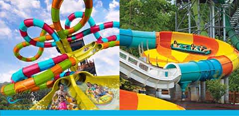 Image of colorful water park slides. On the left, several intertwined slides in vibrant colors with people on a yellow raft sliding down. On the right, a single yellow slide with a double raft carrying two riders enveloped by lush greenery in the background.