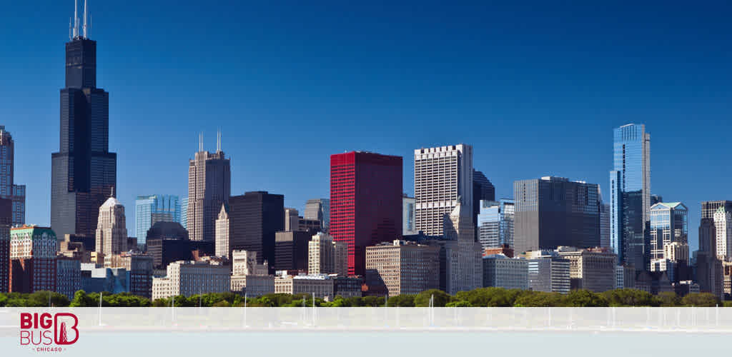 The image shows a panoramic view of Chicago's skyline on a clear day with the iconic Willis Tower standing tallest among an array of skyscrapers. Below the skyline, a Big Bus tour logo suggests sightseeing opportunities in the city.