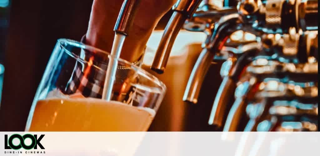 Beer being poured from a tap into a clear glass with blurry background.