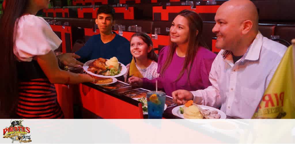 A server presents food to a smiling family seated at a restaurant table.