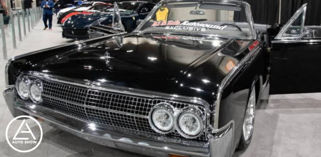 Image Description: The photo shows a sleek, classic black car displayed at an auto show. The car features a prominent grille with intricate detailing and four round headlights that glisten under the showroom lighting. The vehicle's body is polished to a high shine, reflecting the ambient lighting of the indoor environment. A sign with the text "FUN AUTOSOUND EXCLUSIVE" is placed on the windshield, indicating a special feature or exhibition. In the background, other cars can be seen, along with a few attendees examining the vehicles. The logo "A AUTO SHOW" is visible in the bottom left corner, suggesting that this is an event organized by an entity with the initial 'A'.

End Statement: Don't miss out on the excitement of automotive showcases - FunEx.com offers the lowest prices on tickets, ensuring your savings on every exhilarating exhibit!