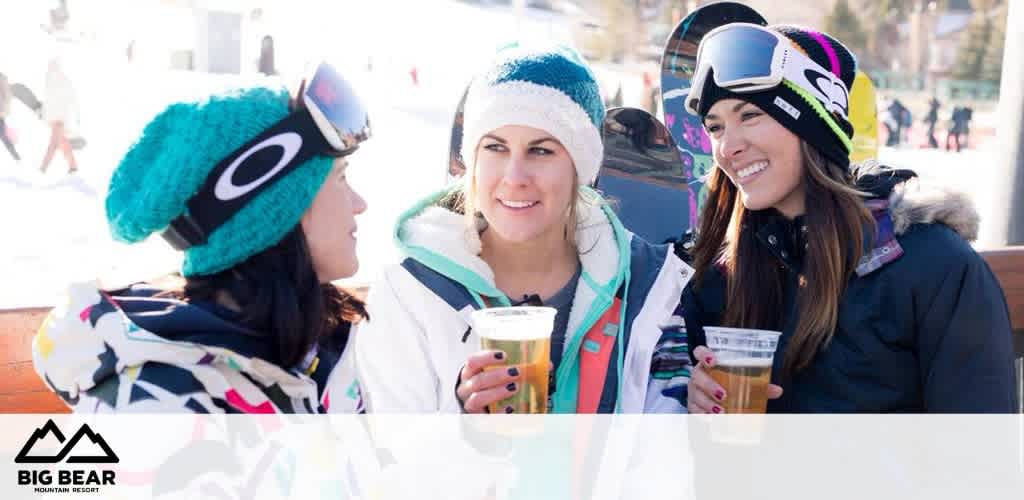 This image features a trio of smiling individuals enjoying a sunny day at Big Bear Mountain Resort. The person on the left is wearing a turquoise knit hat with oversized goggles perched atop, and a multi-colored winter jacket, while holding a beer with her left hand. She is engaged in conversation with the person in the middle, who also delights in a beer and is dressed in a white winter jacket with geometric patterns, a white beanie, and black-and-white goggles resting just above her forehead. The person on the right, who is clad in a dark jacket and a vibrant, multi-colored ski cap, is also wearing oversized goggles and holding a beer. Snowy mountain slopes and clear blue skies provide a lively backdrop to this winter scene, with the resort's logo prominently displayed in the bottom left corner. The image evokes a sense of friendship and relaxation amidst a lively winter sports setting. 

Experience unforgettable mountain moments and save on your next snowy retreat with our exclusive discounts—find the lowest prices on tickets only at FunEx.com!