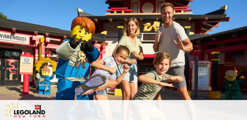 A joyful family poses playfully with a life-sized Lego ninja character at Legoland New York. They mimic martial arts moves under a sunny sky in front of an Asian-inspired structure. Bright Legoland branding is visible.