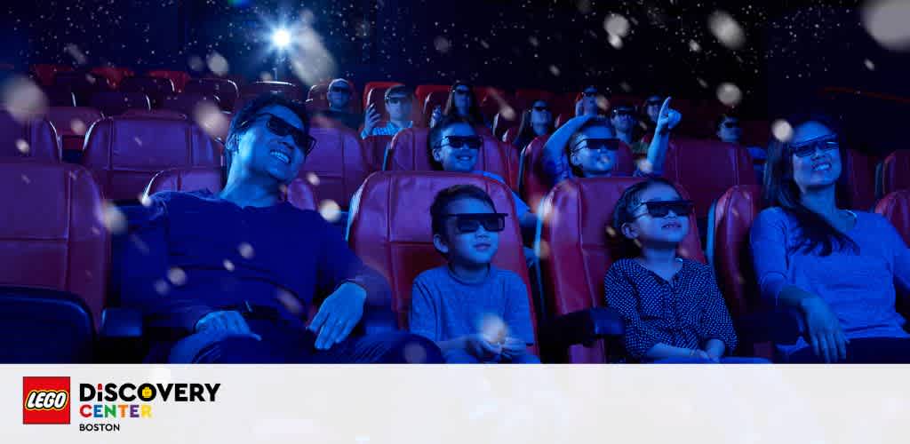 Image depicts a family enjoying a 4D cinema experience at LEGO Discovery Center in Boston. They are seated in red theater chairs, wearing 3D glasses, and looking up at the screen, surrounded by floating light effects indicative of the 4D experience. The LEGO Discovery Center logo is in the top left corner.