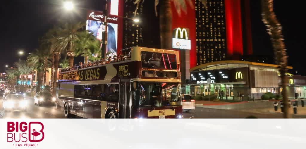 A photo taken at night captures the lively streets of Las Vegas with a 'Big Bus' tour double-decker driving past. In the background are illuminated signage, prominent among them is the golden arches of McDonald's, and the glowing lights of city life.