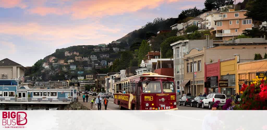 This image features a scenic view of a street in San Francisco during early evening with warm-hued skies above. Two tour buses labeled  Big Bus San Francisco  are visible, one facing towards the viewer. Pedestrians are walking alongside, and a variety of colorful buildings climb up the hill in the background.