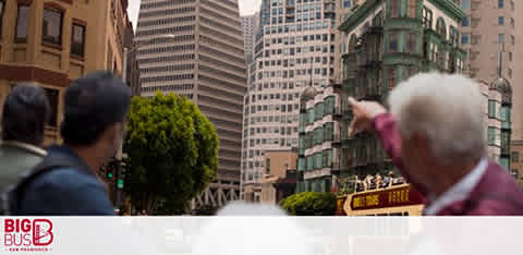 Tourists gazing at city buildings from a bus, with a partly visible "Big Bus" logo.