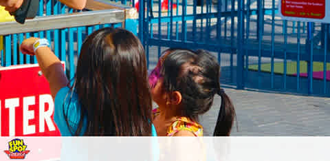 Two kids facing away, pointing at something outside the frame at a colorful outdoor event.