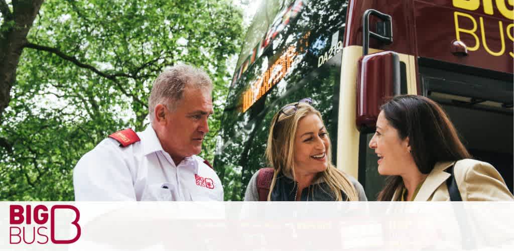 This is an image featuring a Big Bus tour scene. On the left side of the photo, a bus tour guide, who appears professional in a white shirt with red epaulets and a name tag, is seen standing on the steps of a large red double-decker bus, partially visible in the background. The guide seems to be engaged in a conversation. On the right, two smiling women are standing close to each other, one with blonde hair and the other with brunette hair, both casually dressed and looking delighted as they talk. They appear to be potential passengers inquiring about the tour. Lush green trees canopy the background, indicating a pleasant day suitable for sightseeing. In the bottom left corner, the "Big Bus" logo in white and red is clearly visible.

At GreatWorkPerks.com, we're committed to ensuring you get the most out of your travels - enjoy the city's highlights from the open-top deck of a Big Bus and snag the lowest prices on tickets for a variety of attractions, ensuring your adventures are both memorable and affordable!