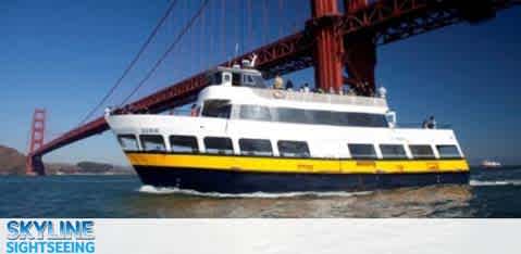 A sightseeing boat cruises under a large red bridge on a sunny day.