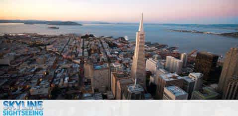 Aerial view of a city skyline at dusk, featuring a tall spire building, with water in the distance.