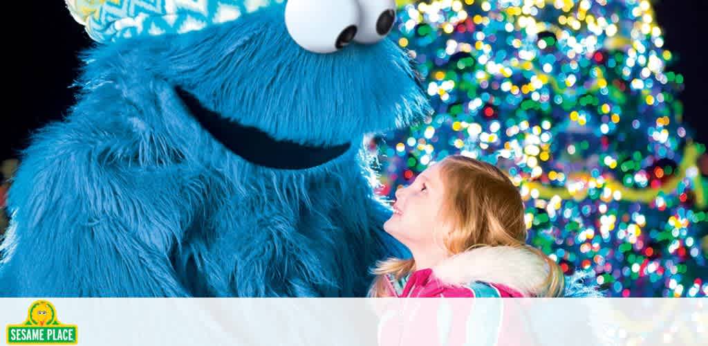 A child gazes up at a blue furry character with a twinkling tree in the background.