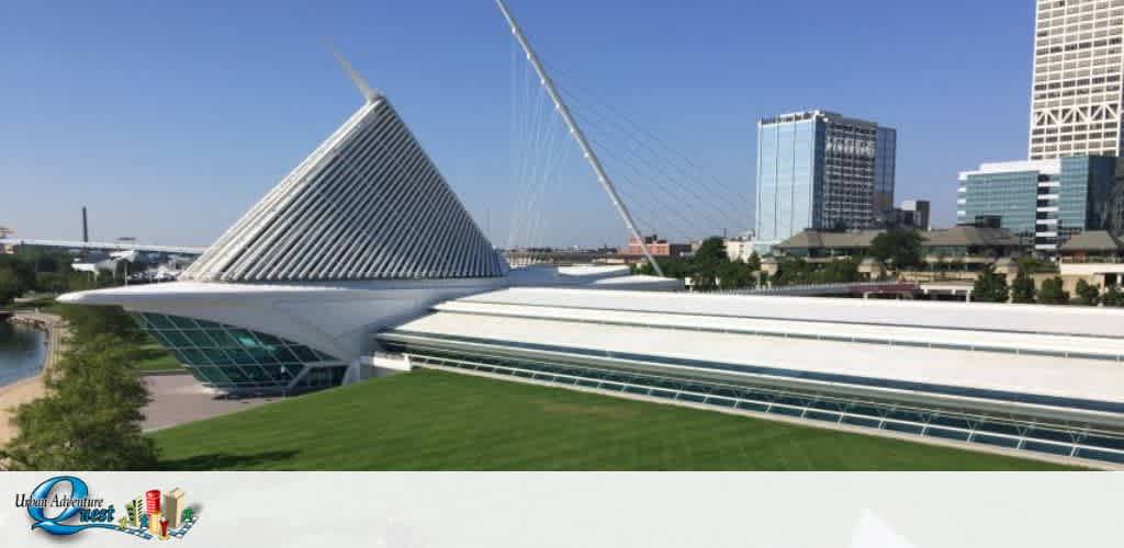 Image depicts a modern building with a prominent, cone-shaped structure with a white, sloped roof. It's part of a complex with multiple buildings, a suspension bridge on the right, and greenery in the foreground. The background showcases a clear sky and city skyline. The Urban Adventure Quest logo is at the bottom left.