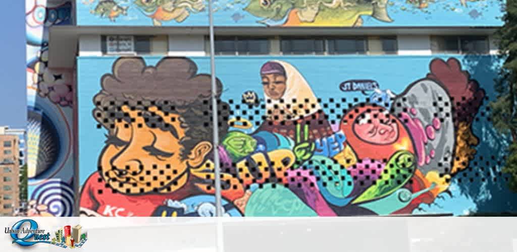 The image shows a vibrant mural with various stylized characters, including a smiling figure with exaggerated features in the foreground, and a depiction of a person with a headscarf in the background. The artwork is colorful, with a mix of patterns, shapes, and text elements. The mural is on the side of a building with visible windows reflecting the sky.