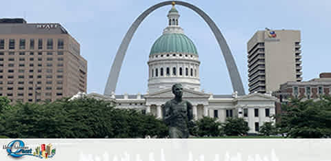 Image shows a cityscape with the iconic Gateway Arch in the background and a dome-capped building resembling a Capitol in the foreground. In front of the Capitol a statue can be seen, and there are modern buildings to the left. The sky is overcast.