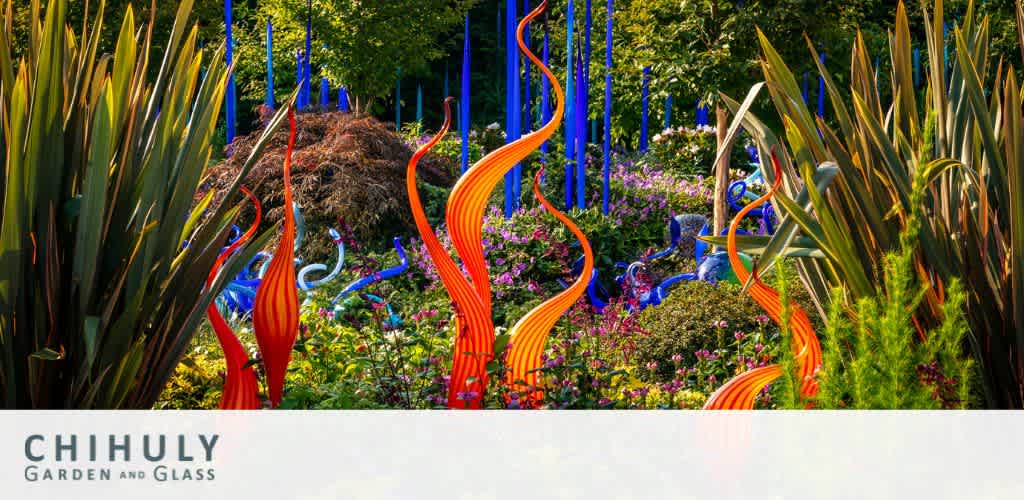 Image shows a vibrant garden from Chihuly Garden and Glass with a mix of lush greenery and striking glass sculptures. Tall blue rods and swirling orange and red shapes stand out amidst the foliage under a clear blue sky.