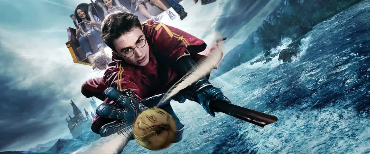 An exhilarating scene showcasing a young wizard riding a broomstick over a turbulent ocean. He's clad in a maroon and gold outfit, intently chasing a golden ball. Behind him, other ride-goers are enjoying an amusement park attraction, all against a dramatic backdrop featuring a stormy sky and a distant castle.