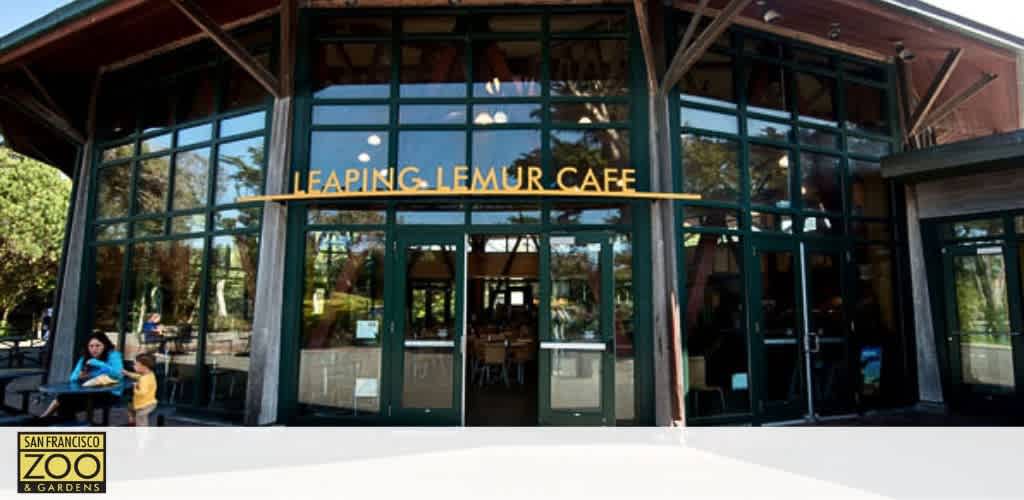 Front view of the Leaping Lemur Cafe at the San Francisco Zoo & Gardens. It's a large wooden structure with glass doors and windows. The cafe's name is displayed in bold letters above the entrance. Visitors are visible outside the building.