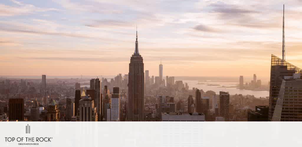 Image displays a panoramic view of New York City's skyline at sunset. The Empire State Building dominates the scene centrally, with a myriad of skyscrapers surrounding. A warm glow bathes the city, the sky fades from a soft orange to a gentle blue, and the Hudson River is visible in the distance. Text overlaid at the bottom reads  Top of the Rock Observation Deck. 