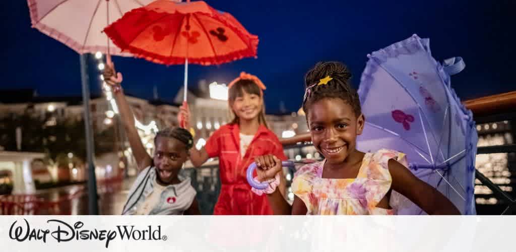 Three children smile and dance under colorful umbrellas at night in a lively and joyful setting. They wear bright clothing, adding to the festive atmosphere. In the background, lights twinkle, creating a warm ambiance. A large building with lit windows is visible, enhancing the scene's whimsical charm. The image evokes feelings of fun and delight, capturing a memorable moment of celebration and playfulness.