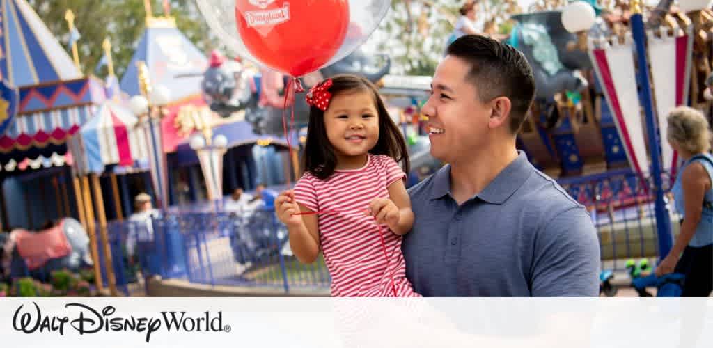 A joyful young girl in a red and white striped dress holds a red balloon while being carried by an adult wearing a blue shirt. They are both smiling happily. The background features a colorful theme park ride and festive decorations, conveying a fun and lively atmosphere.