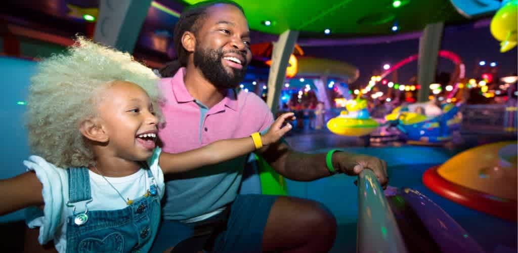 A man and child enjoy a colorful amusement park ride at night. The scene is filled with bright lights and a vibrant atmosphere, with the child laughing and holding onto the ride's rail. The background features various amusement rides and glowing decorations, creating a festive and joyful mood.