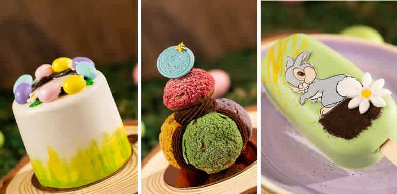 Three colorful desserts with a spring theme are displayed. The first is a white cake topped with pastel eggs and green detailing. The second is a tower of macarons in various colors, including a blue coin accent. The third is a green popsicle with a cartoon rabbit and flower decoration, laid on a purple plate. The background is blurred with earthy tones.