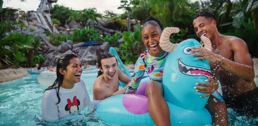 A group of four diverse friends enjoys a fun day at a water park. They laugh and splash in a lazy river, with one person riding a colorful inflatable monster float. The lush greenery in the background adds to the tropical atmosphere, creating a joyful and vibrant scene that highlights friendship and leisure.