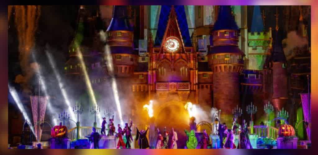 A vibrant nighttime show in front of a majestic castle with blue spires features performers in colorful costumes and dramatic lighting effects. Bright spotlights and bursts of flame are part of the spectacle, enhancing the magical and festive atmosphere. Decorative elements, including illuminated pumpkins, adorn the scene, creating a lively and enchanting experience.