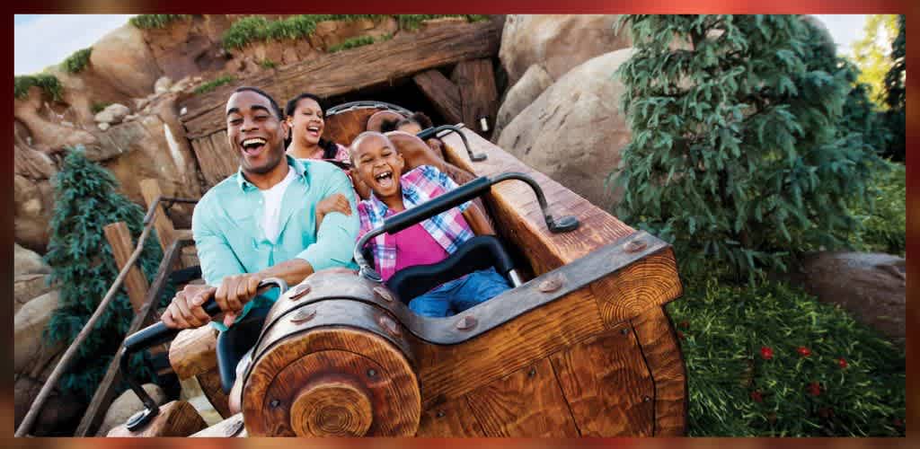 A family enjoys a thrilling ride on a wooden roller coaster, laughing and smiling as they soar through a scenic landscape with rocky terrain and greenery. The front view captures their excitement and joy, creating a sense of adventure and fun.