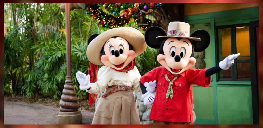 Two iconic cartoon characters in safari outfits, posing together in an outdoor setting with lush greenery and colorful decorations in the background. One character wears a wide-brimmed hat and a red scarf, while the other sports a smaller hat and red shirt. Both are smiling, creating a joyful and welcoming scene.