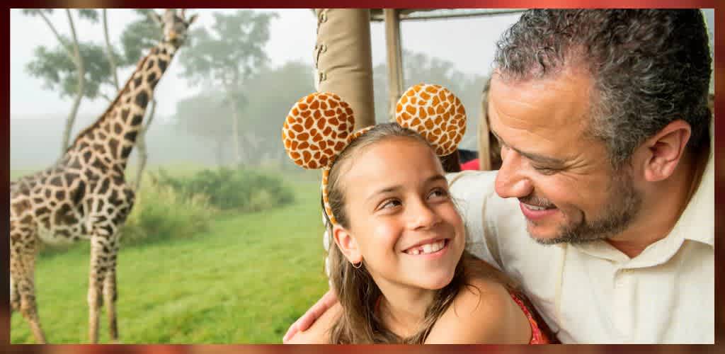 A joyful moment captured at a safari adventure shows a young girl with giraffe-patterned headband smiling broadly at an adult male. In the background, a giraffe stands amidst lush greenery, providing a sense of wonder and excitement. The pair share a warm embrace, highlighting a memorable family experience in a vibrant and natural setting.