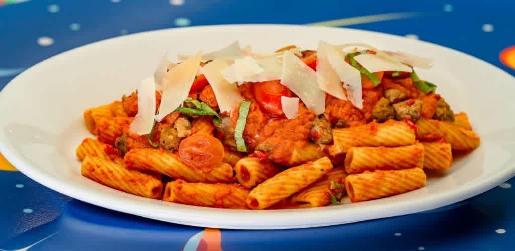 Plate of cooked pasta with tomato sauce topped with shredded cheese green herbs and small pieces of meat
